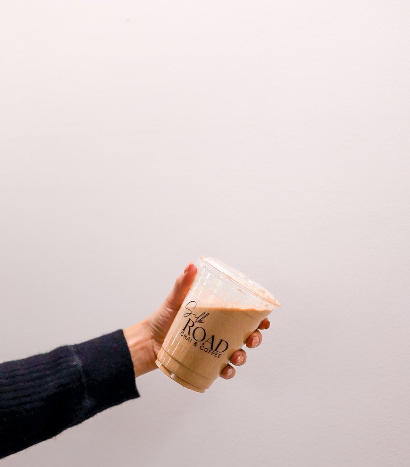 A hand holding a Silk Road iced coffee cup